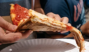 hand holding a folded slice of New York style pizza