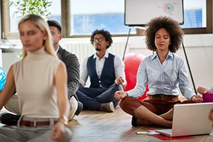group of coworkers sitting on the floor meditating together.