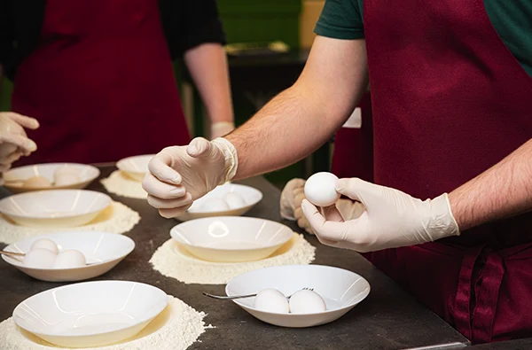 photo of close-up of gloved hands holding eggs during a culinary class