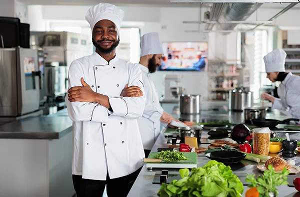 photo of gastronomy expert standing in restaurant professional kitchen with arms crossed while smiling at camera