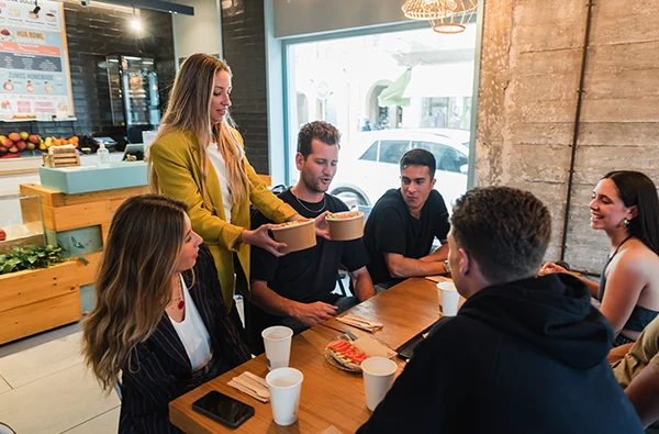photo of a woman bringing food to group of friends in cafeteria