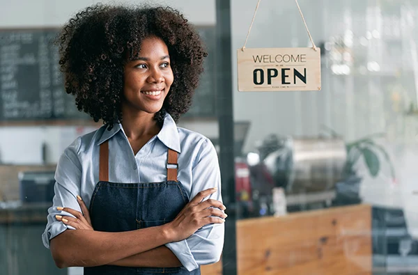 photo of smiling woman leaning next to a welcome sign