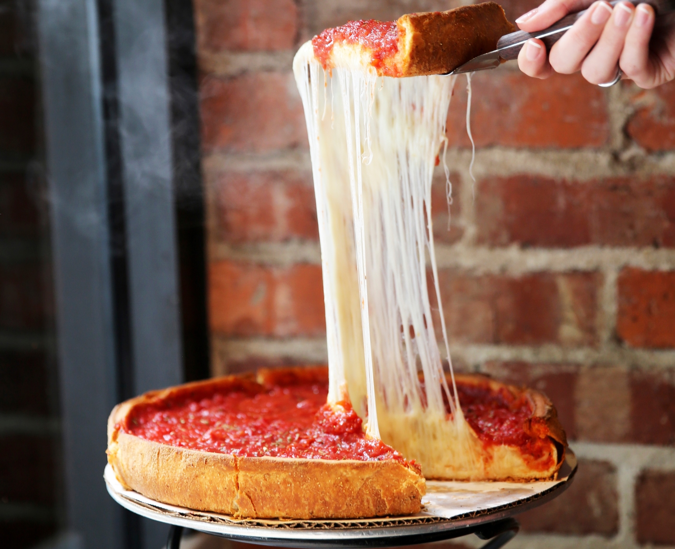 Slice of deep dish pizza being cut and lifted from pizza with intense cheese pull