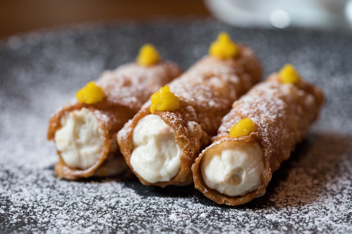 3 cannolis on a plate dusted with powdered sugar
