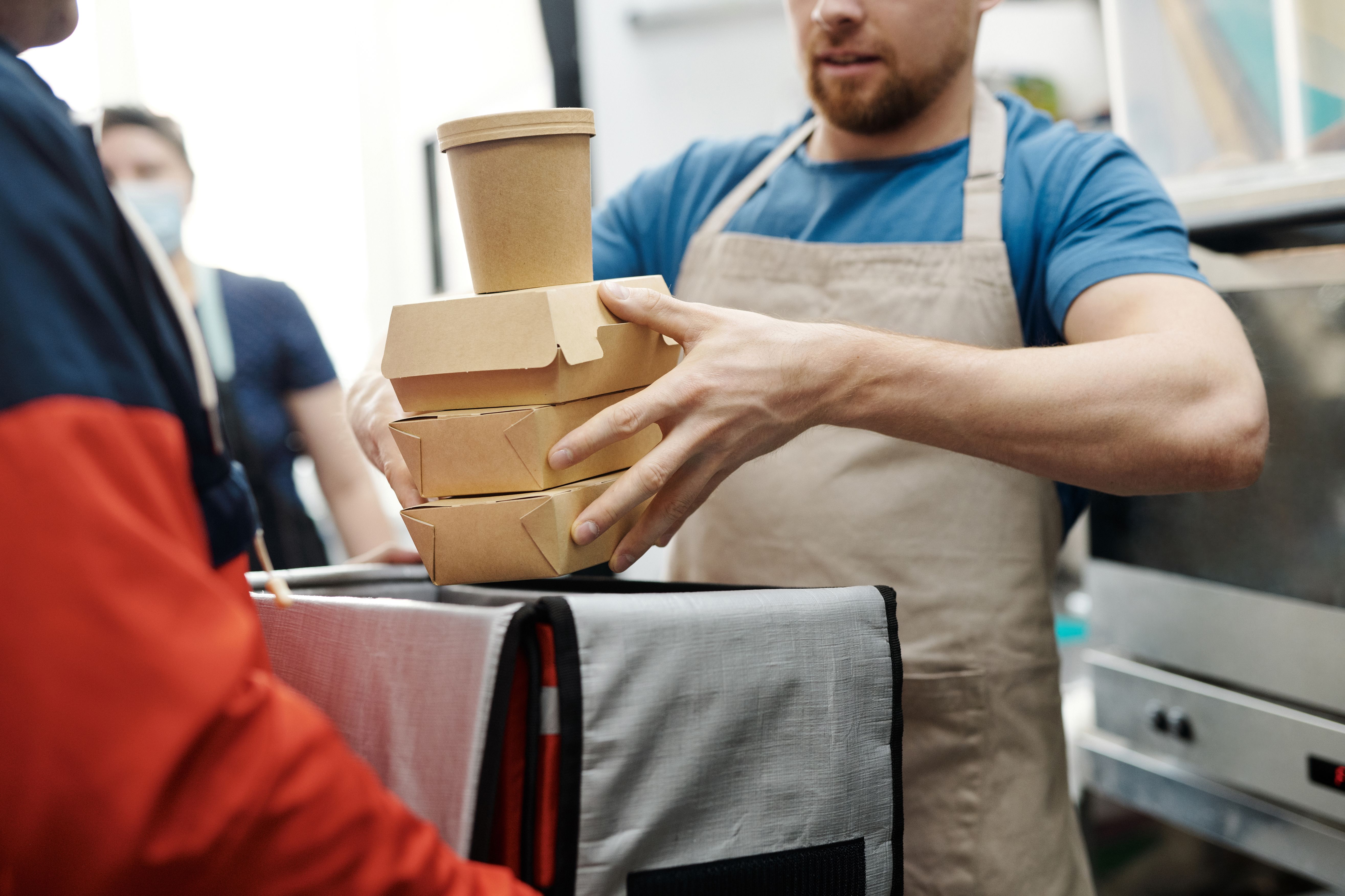 Restaurant worker putting delivery orders in a delivery driver's bag