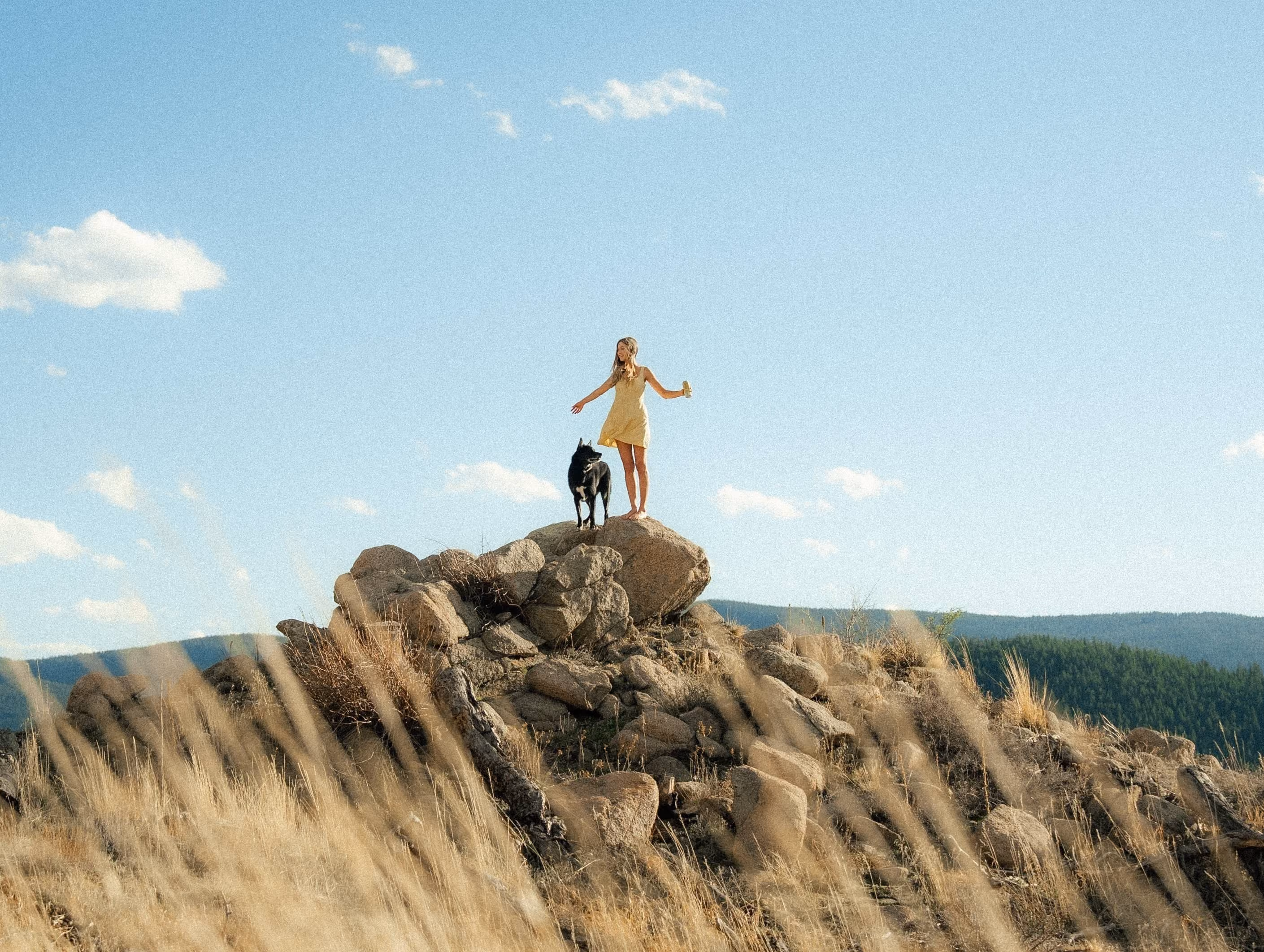 Props creator standing on a rocky hilltop with her dog under a wide blue sky