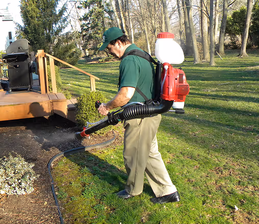 Commercial pest control technician applying outdoor treatment with backpack sprayer as part of hotel pest control services.
