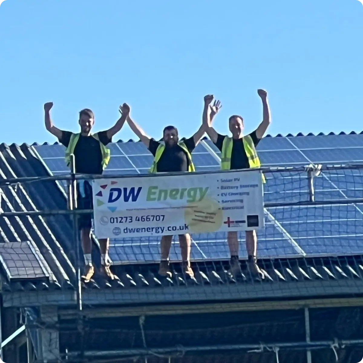 Three workers in yellow vests celebrating on a roof with solar panels and a DW Energy banner.