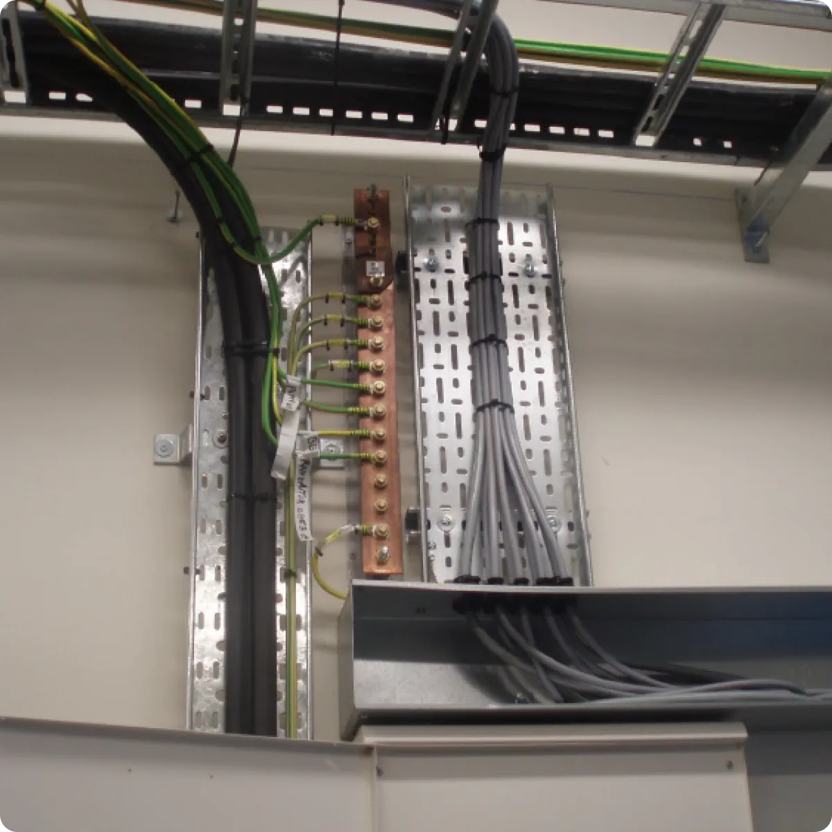 Electrical wiring with green-yellow earth wires on copper busbar and gray cables tied on metal panels.