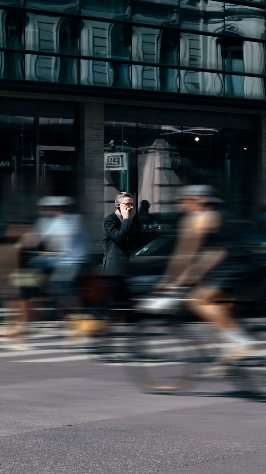 Ein Mann im Anzug telefoniert auf einem städtischen Zebrastreifen, während Radfahrer vorbeifahren.