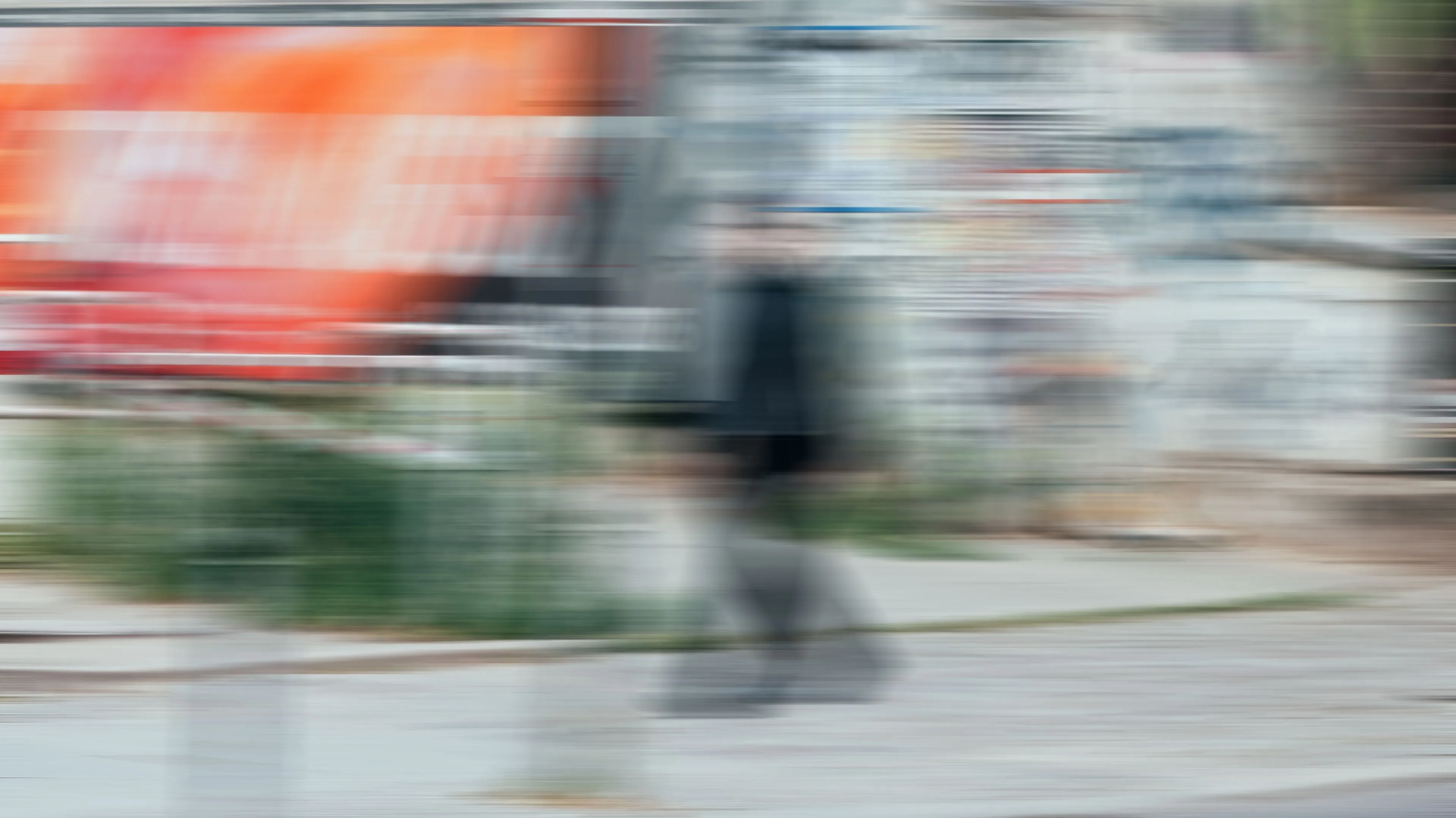Verwischtes Bild einer Person in schwarzer Kleidung, die auf einem Bürgersteig vor einer mit Graffiti bedeckten Wand geht.