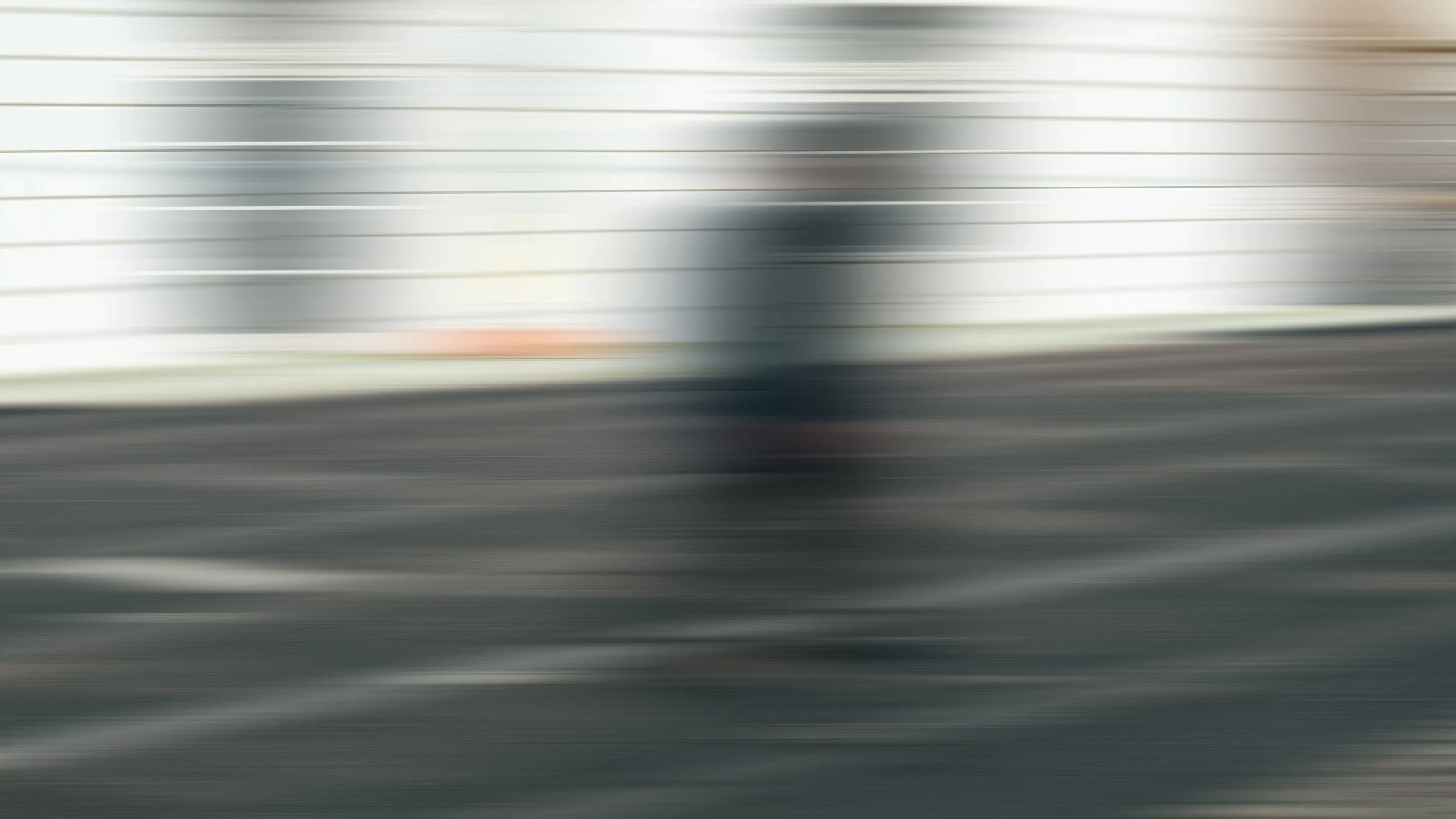 Verschwommenes Bild einer Person, die vor einem weißen Gebäude auf einem Parkplatz steht.