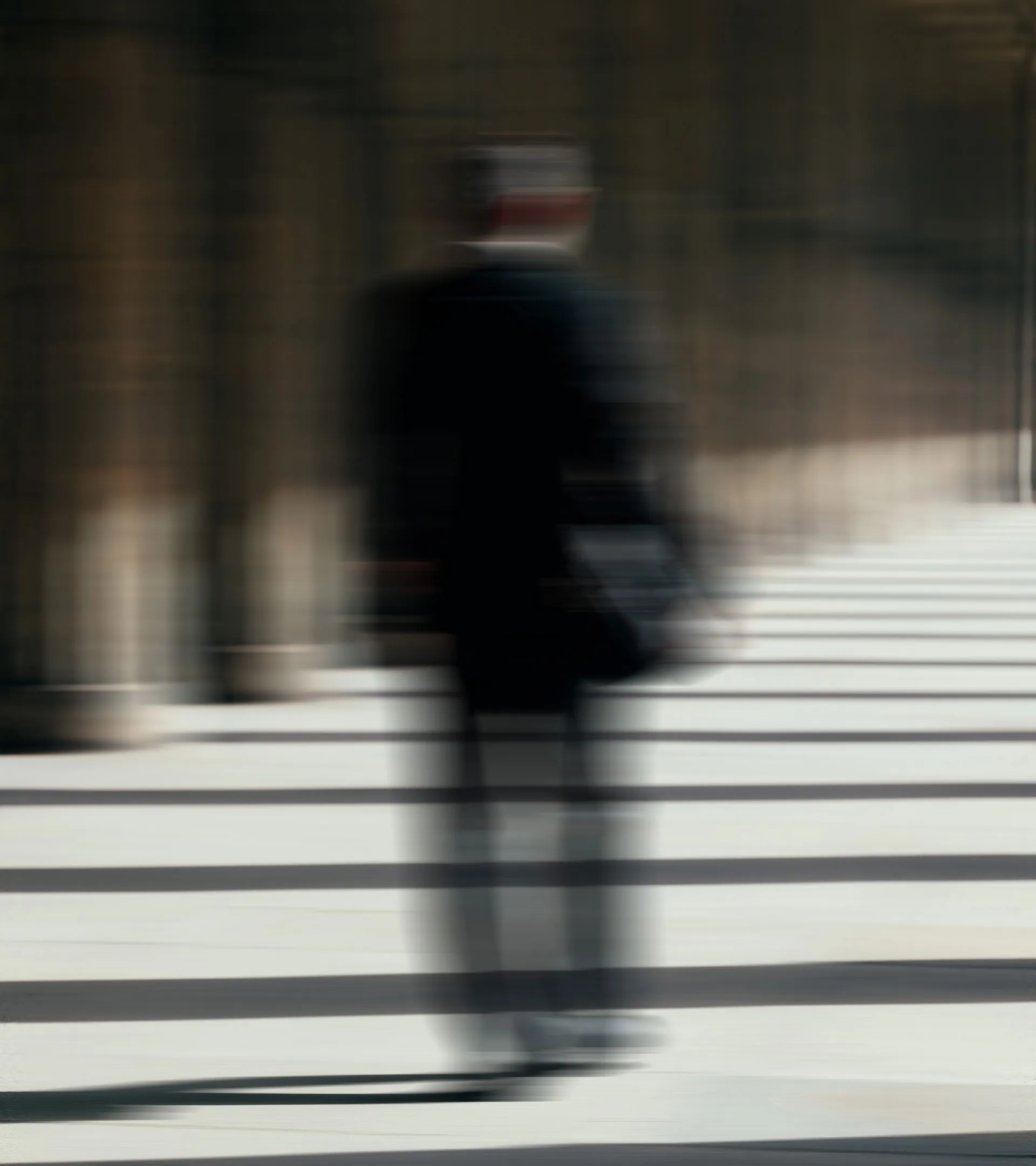 Verschwommene Silhouette einer Person, die in einem Säulengang mit hellem Boden und Schatten zwischen den Säulen läuft.