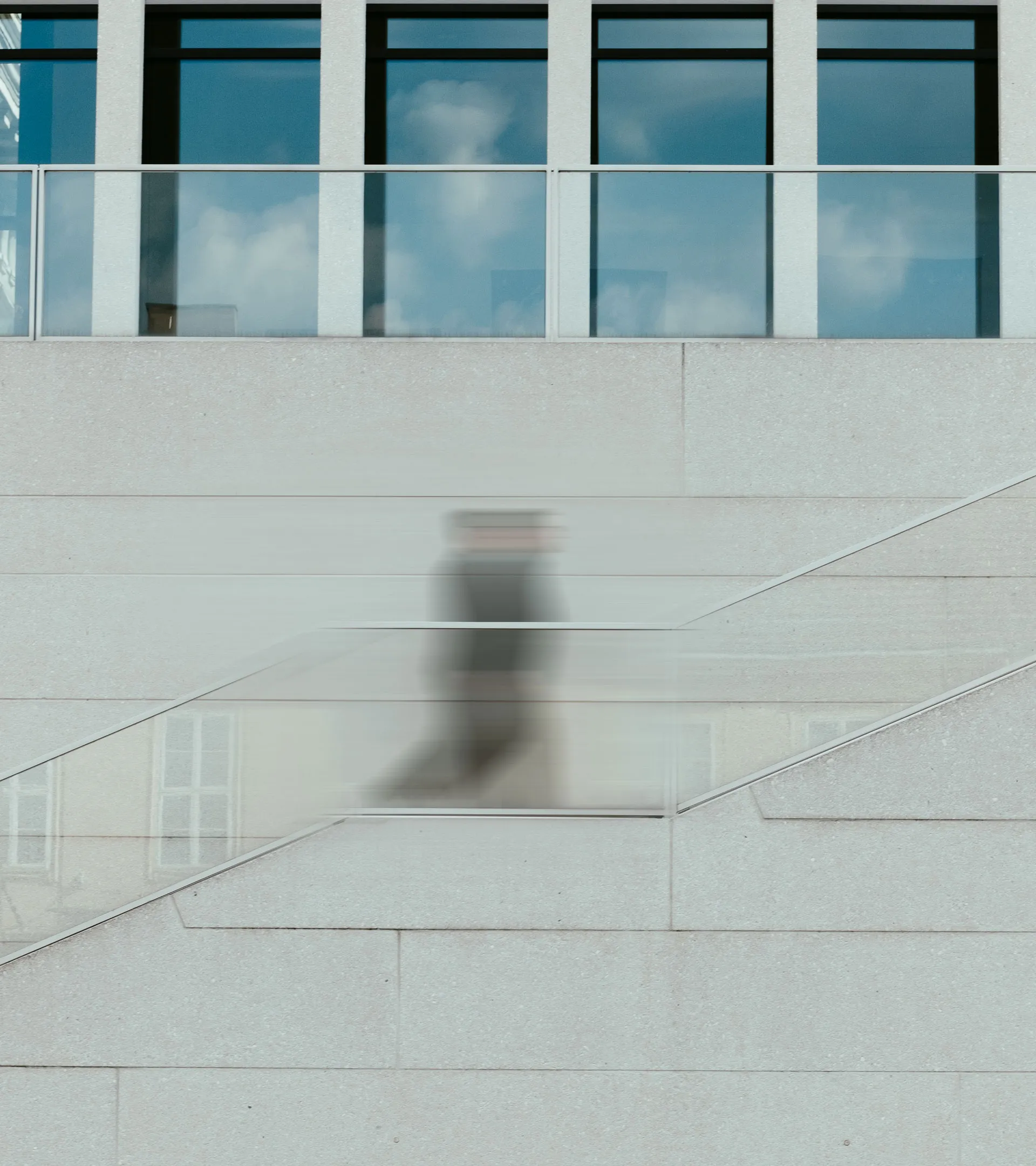 Verschwommene Person läuft eine Treppe mit Glasgeländer vor einem modernen Gebäude mit großen Fenstern hoch.