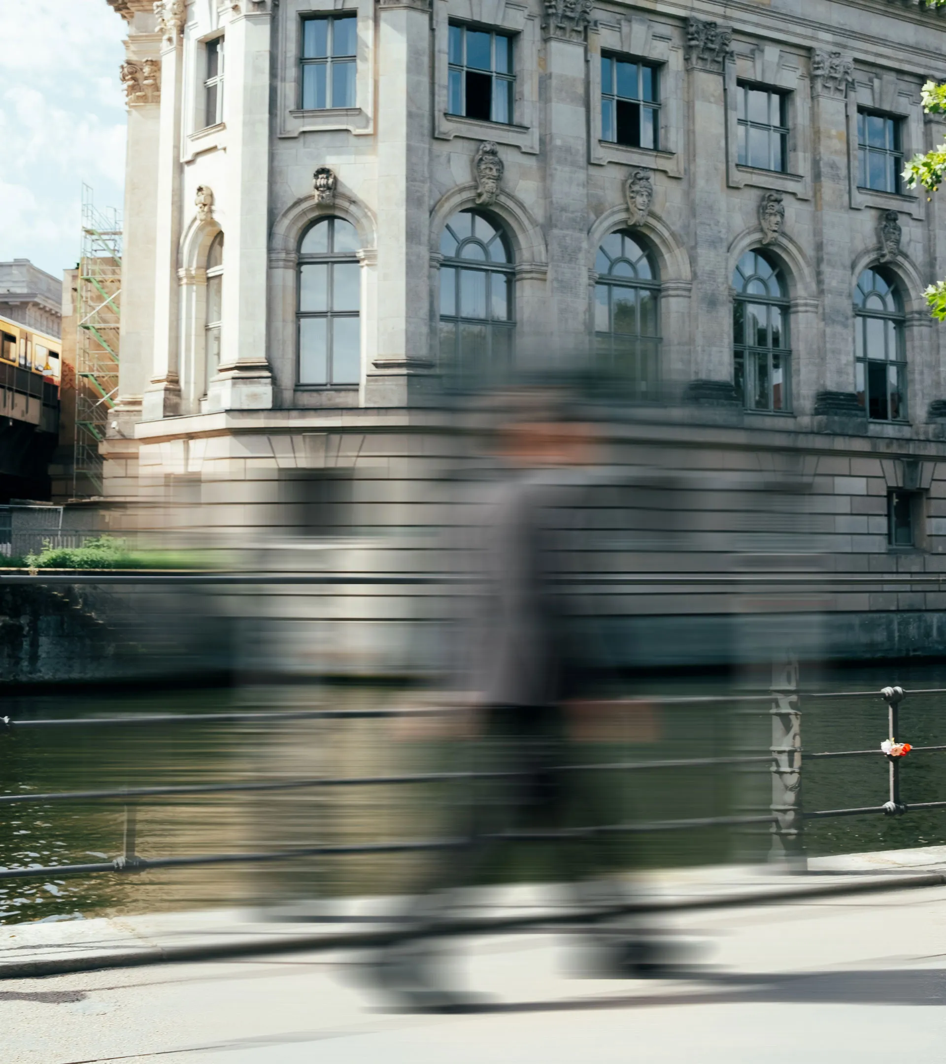 Verschwommene Figur einer Person, die an einem Flussufer mit Geländer entlang einer historischen Steinarchitektur geht.