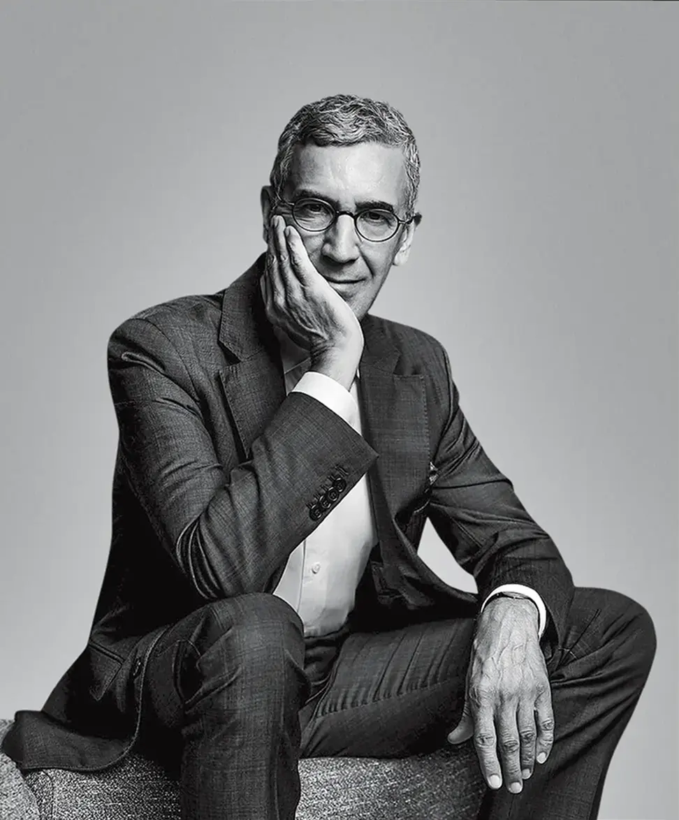 Black and white portrait of Antonio in tailored suit and glasses, one hand resting against his face