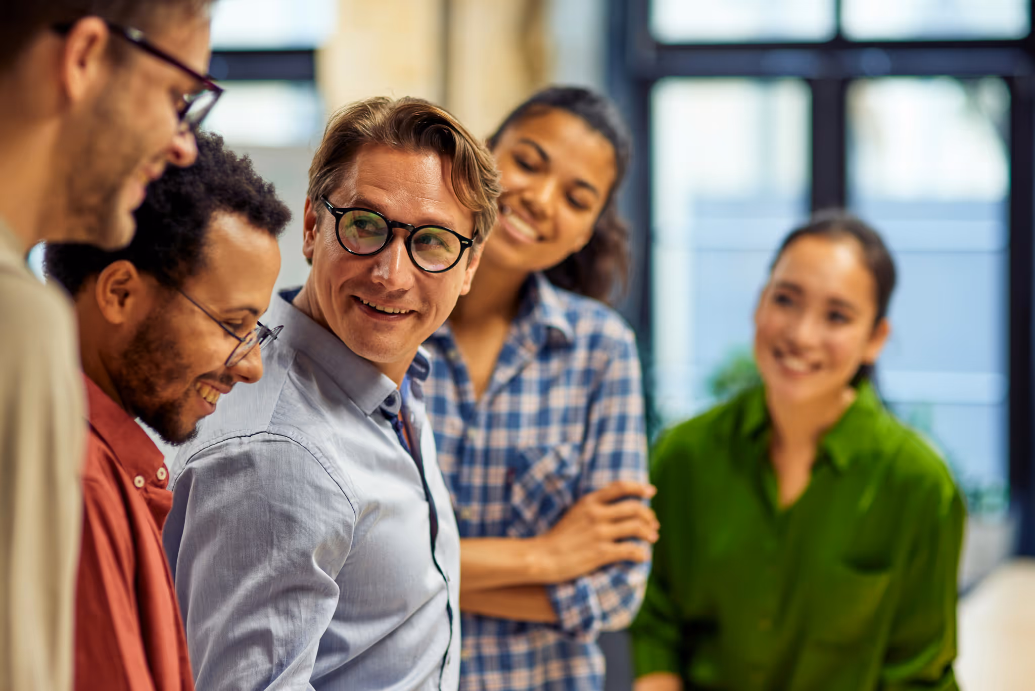 Five diverse colleagues smiling and engaging in a friendly conversation in a modern office.