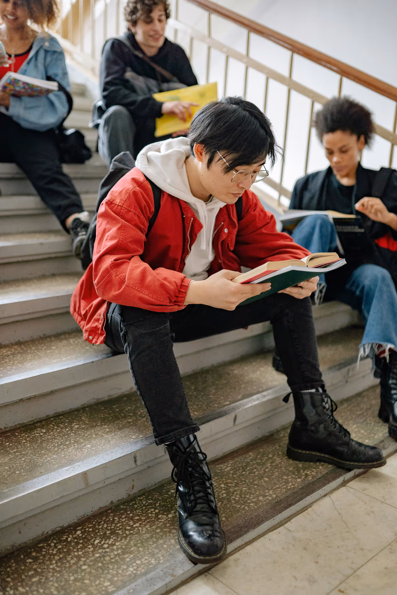Young diverse students sitting on indoor stairs reading books and studying together.