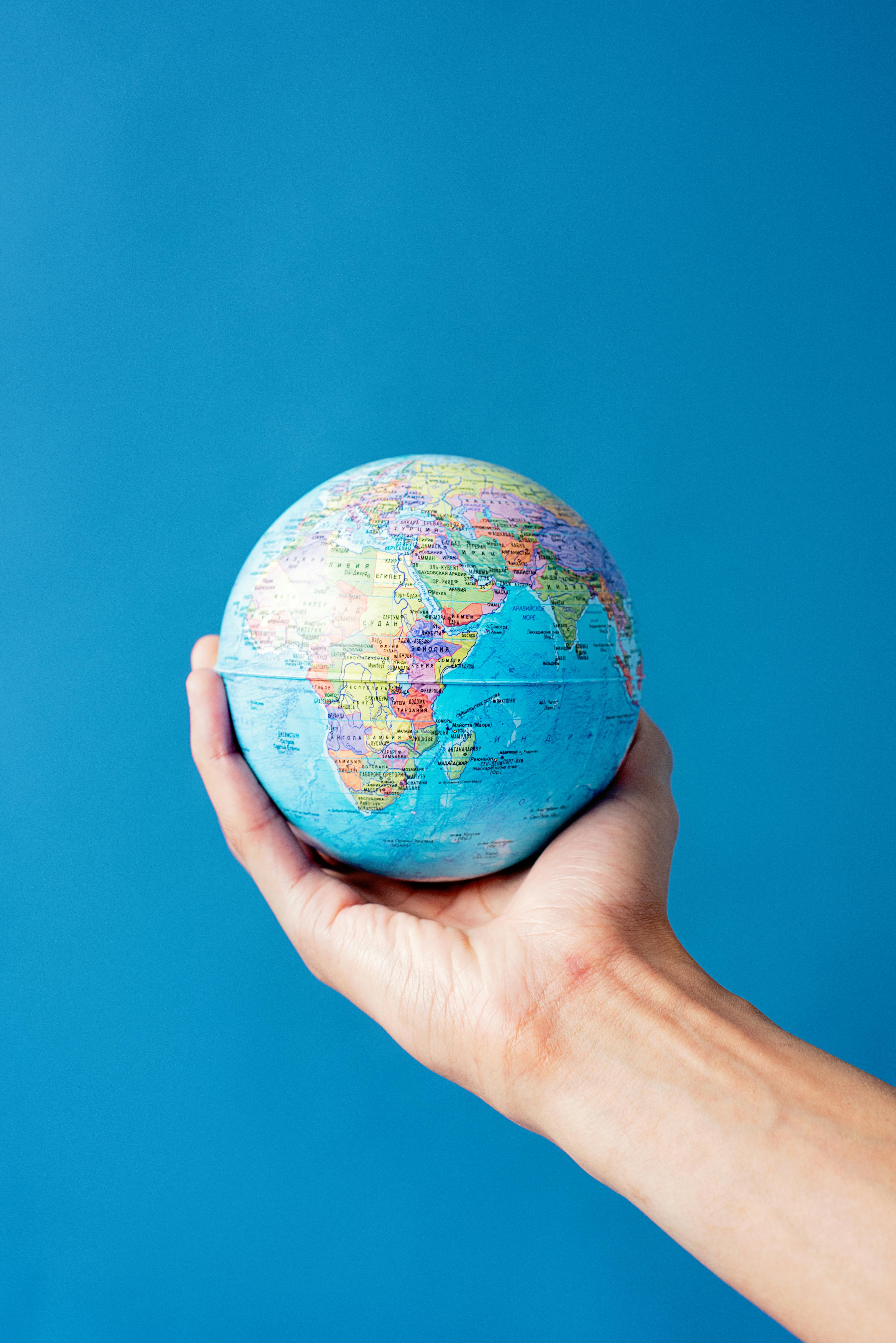 Hand holding a small globe showing Africa, the Middle East, and parts of Europe and Asia against a blue background.