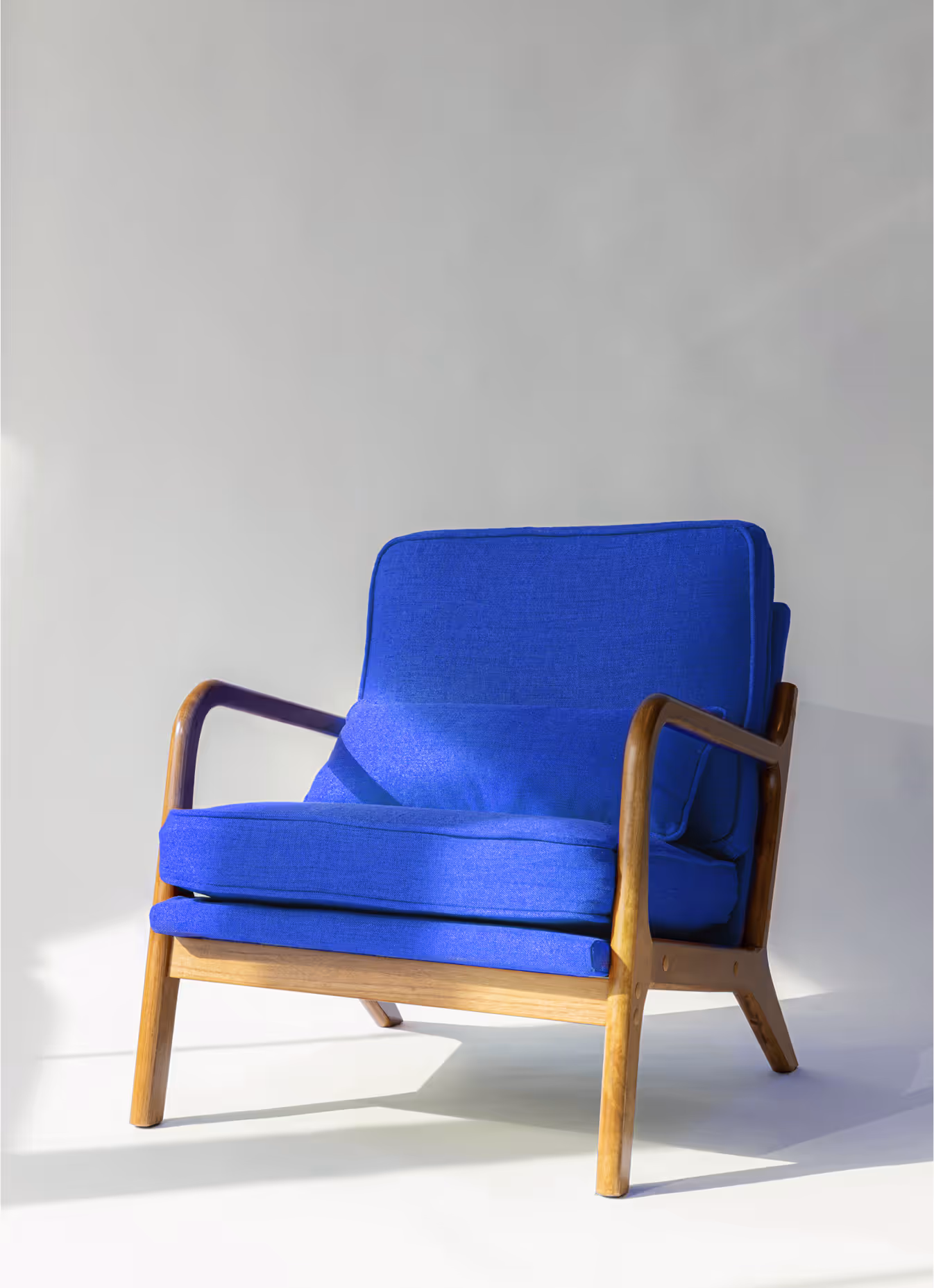 Modern armchair with bright blue cushions and a wooden frame against a plain light background.