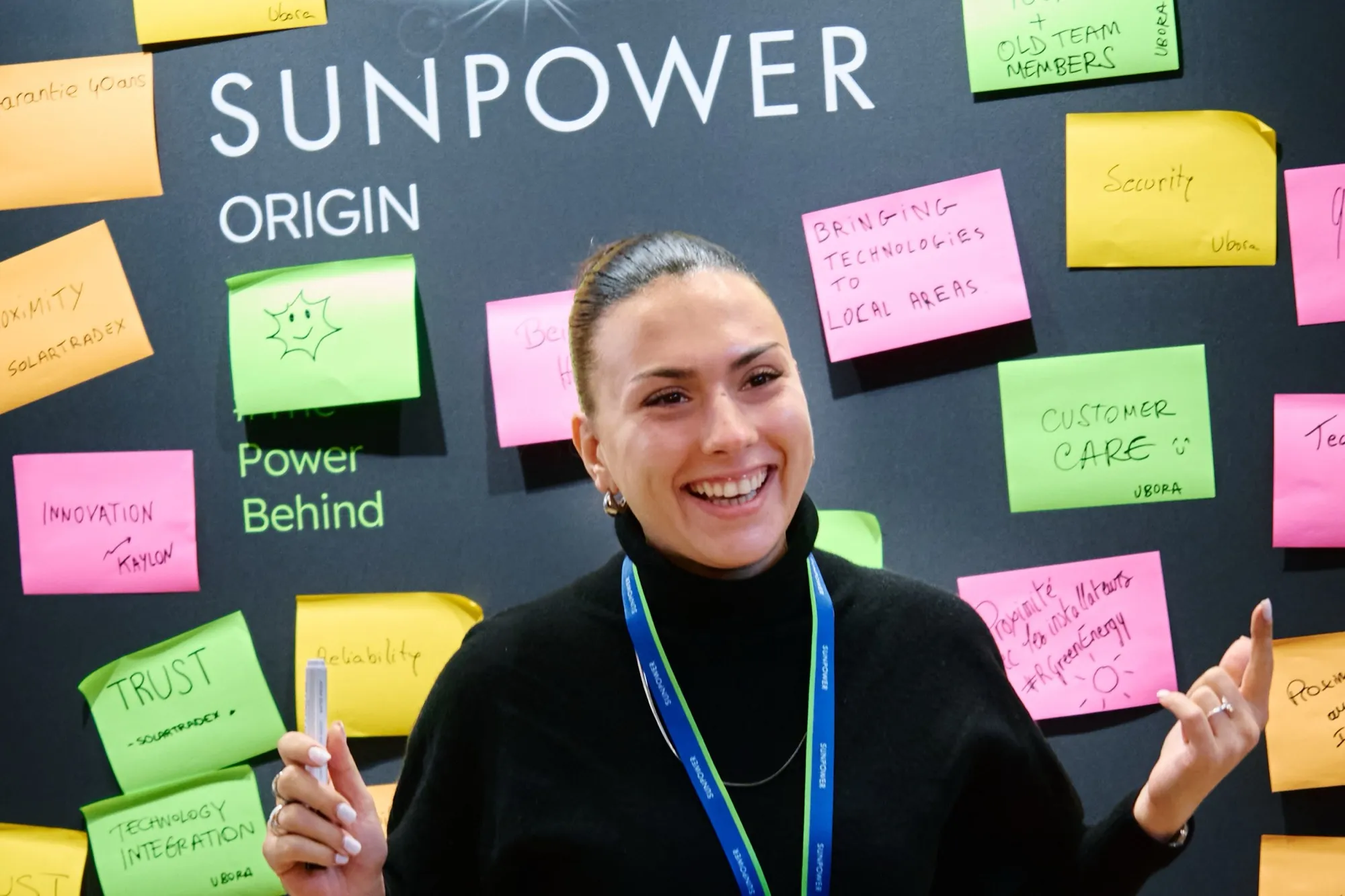 A SunPower Partner laughing in front of a SunPower Origin The Power Behind wall covered in sticky notes