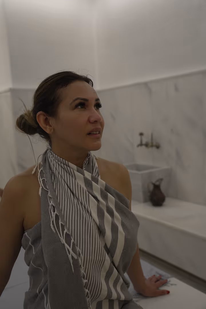 Escarle Silva wrapped in a striped towel sitting in a marble room, looking upward.