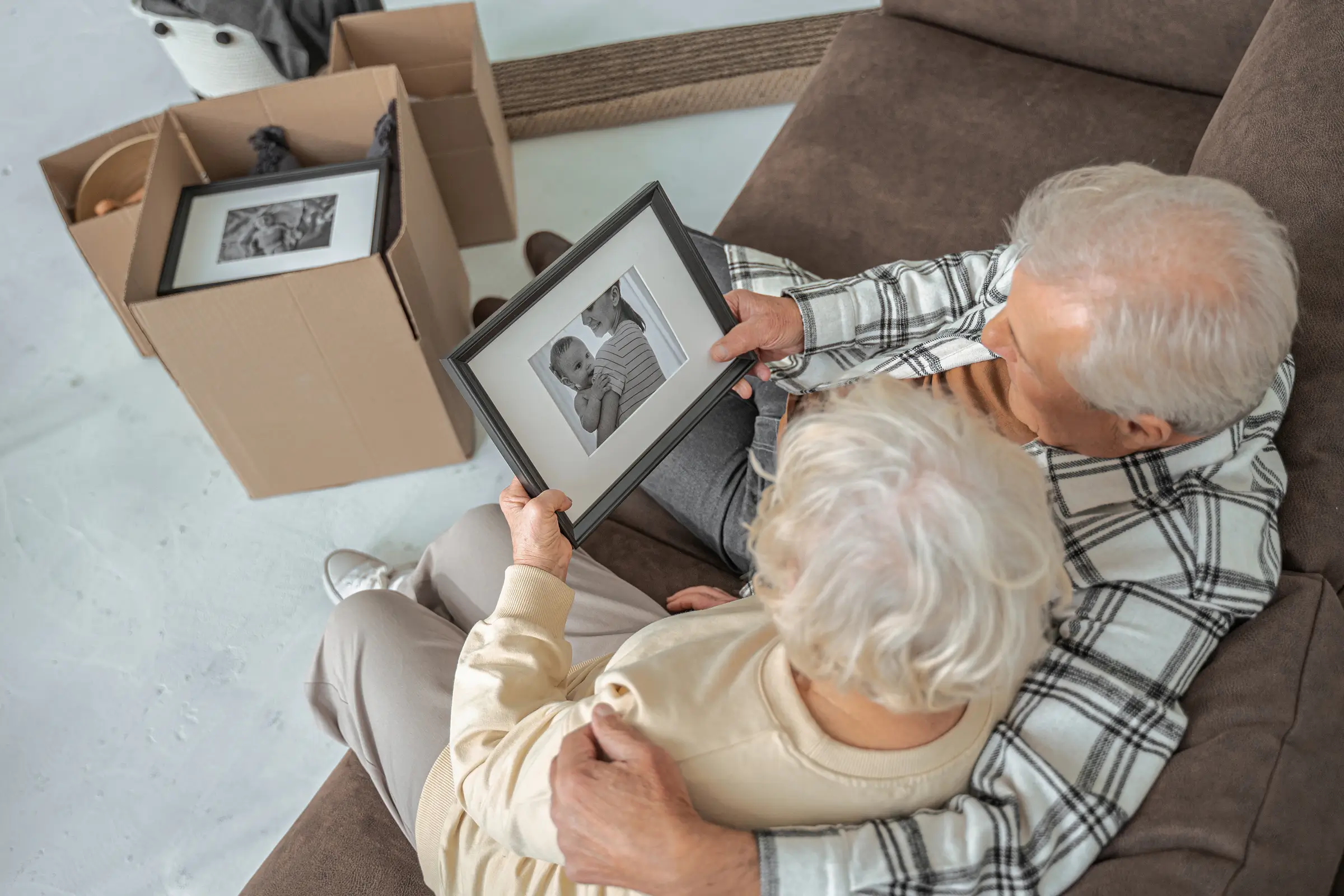 Elderly couple sitting on the couch looking at a box of framed photos. 