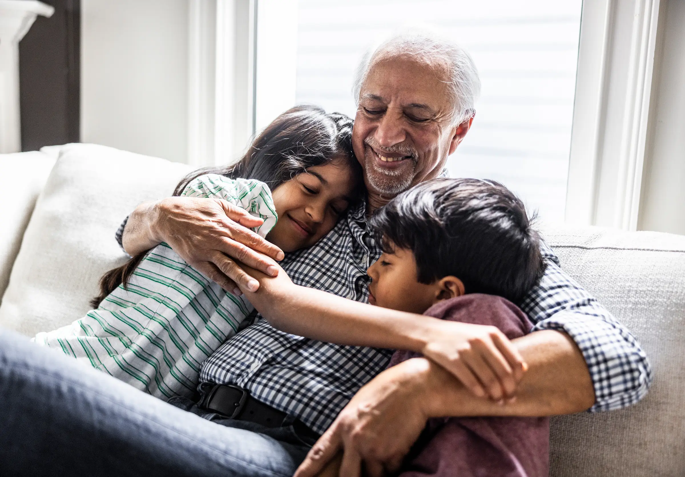 Middle aged man sits and hugs his grandchildren as he cherishes the moment of being with family.
