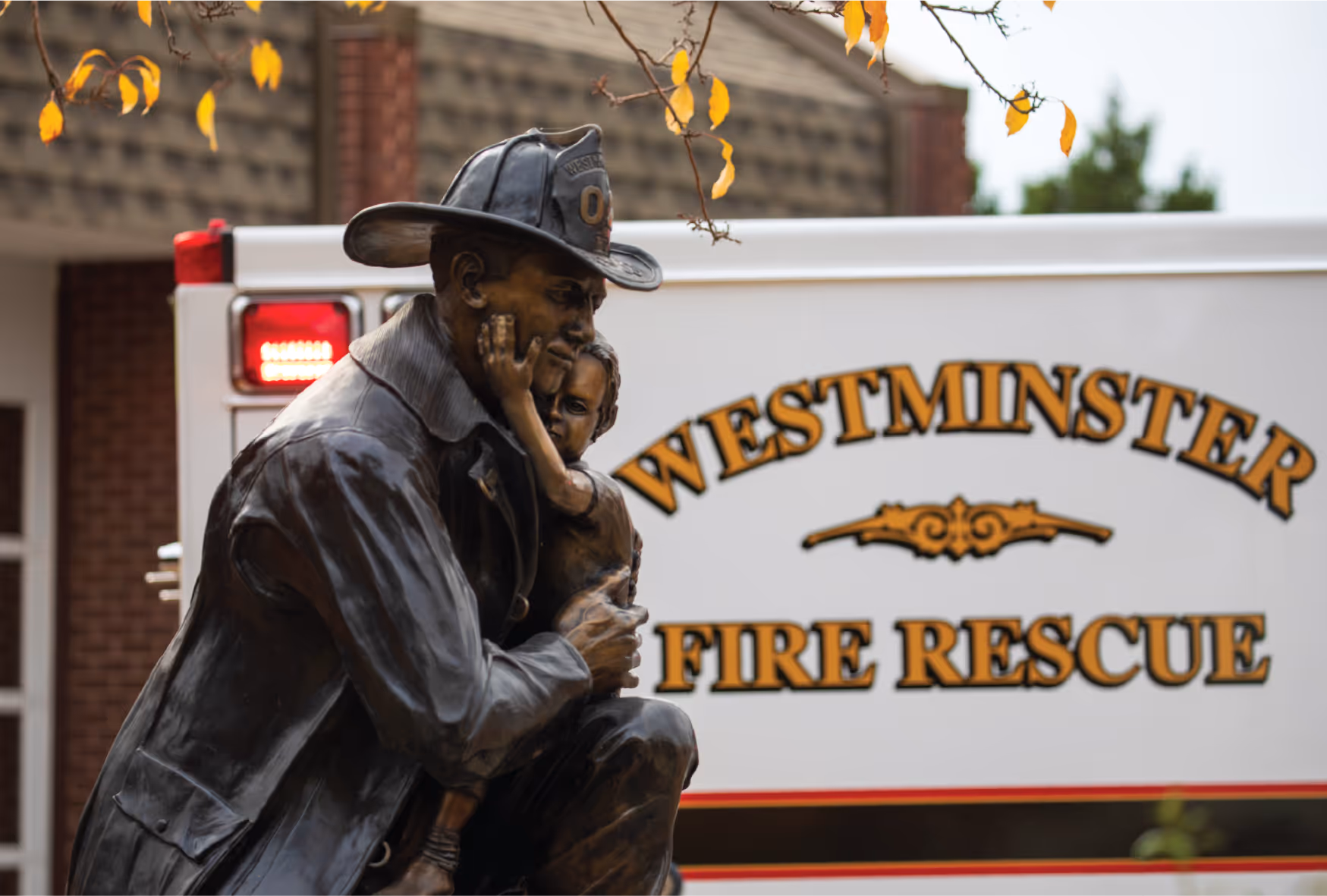 Statue of a firefighter holding a child in front of a Westminster Fire Rescue emergency vehicle.