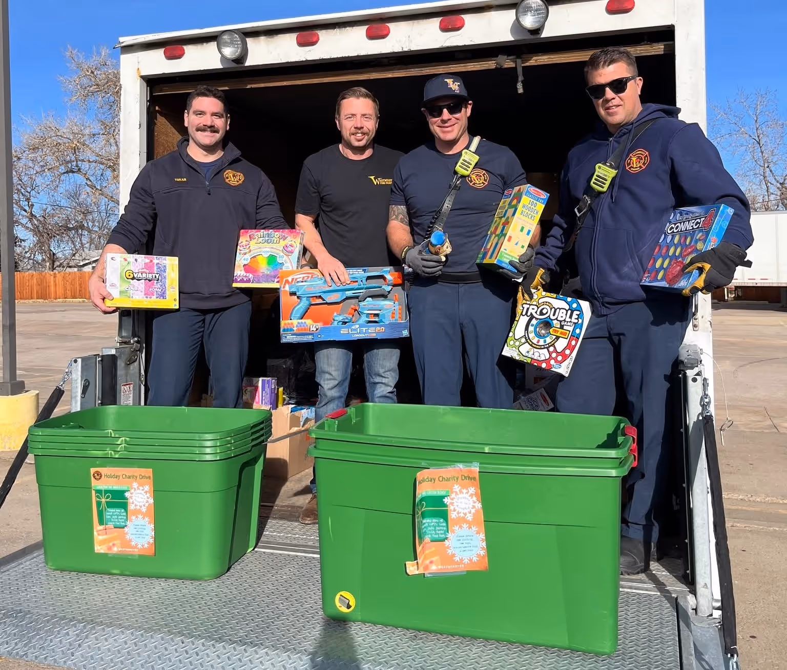 Firefighters standing at the back of a truck holding donated toys for a holiday toy drive.