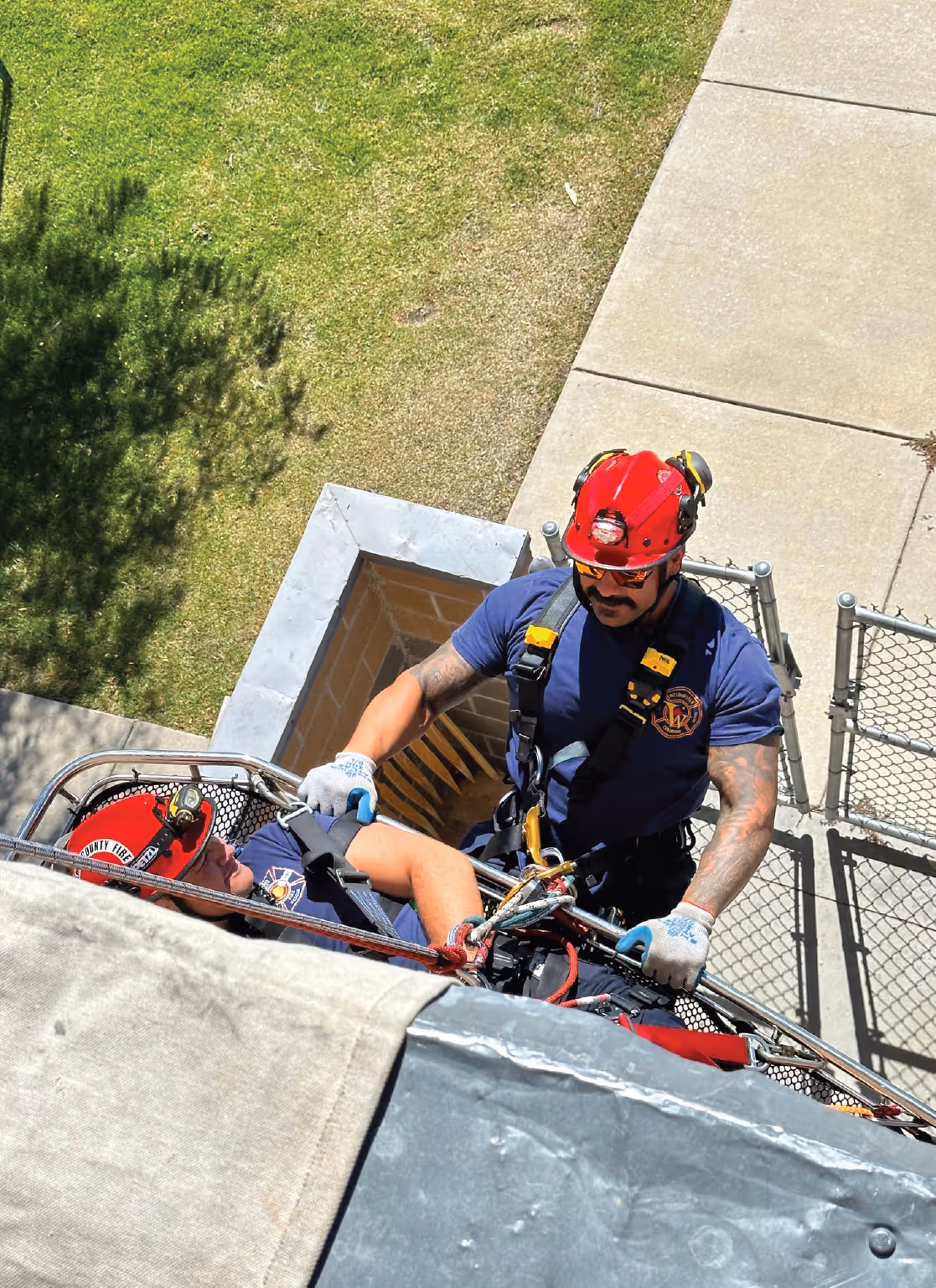 Firefighter in safety gear assisting with a rooftop rope rescue training exercise.