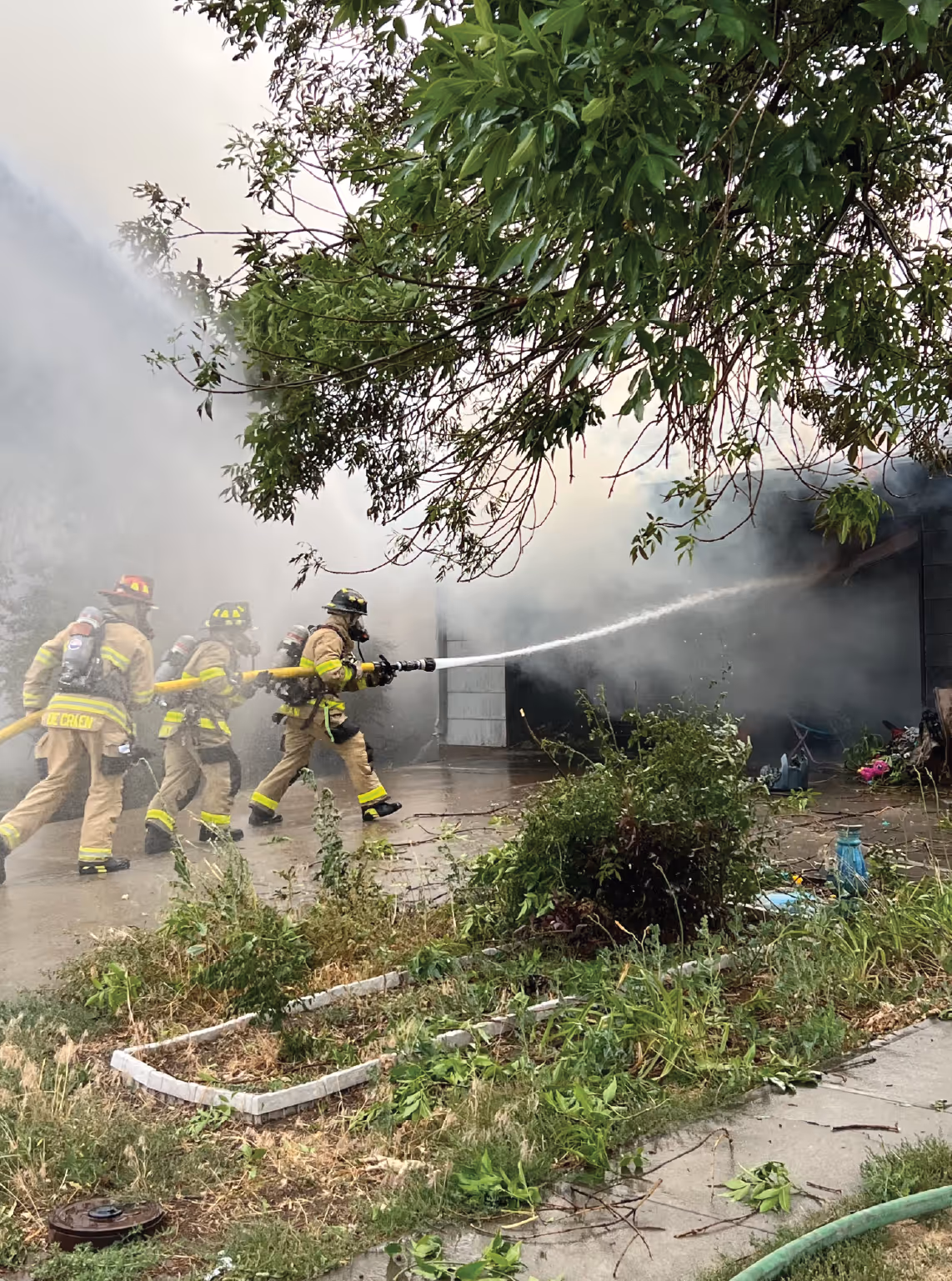 Firefighters in full gear extinguishing a house fire with heavy smoke.