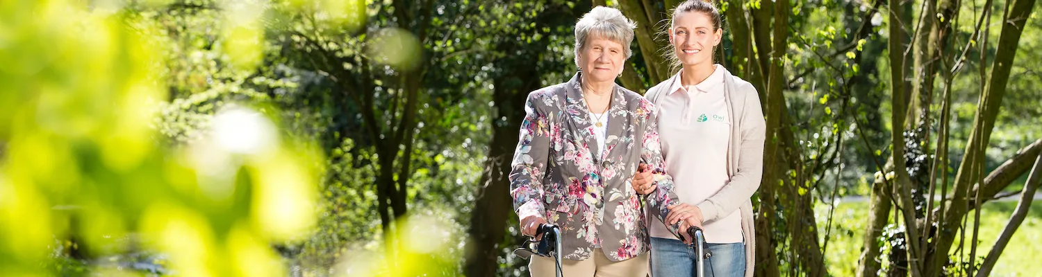 Seniorin steht im Grünen und schaut freundlich in die Kamera
