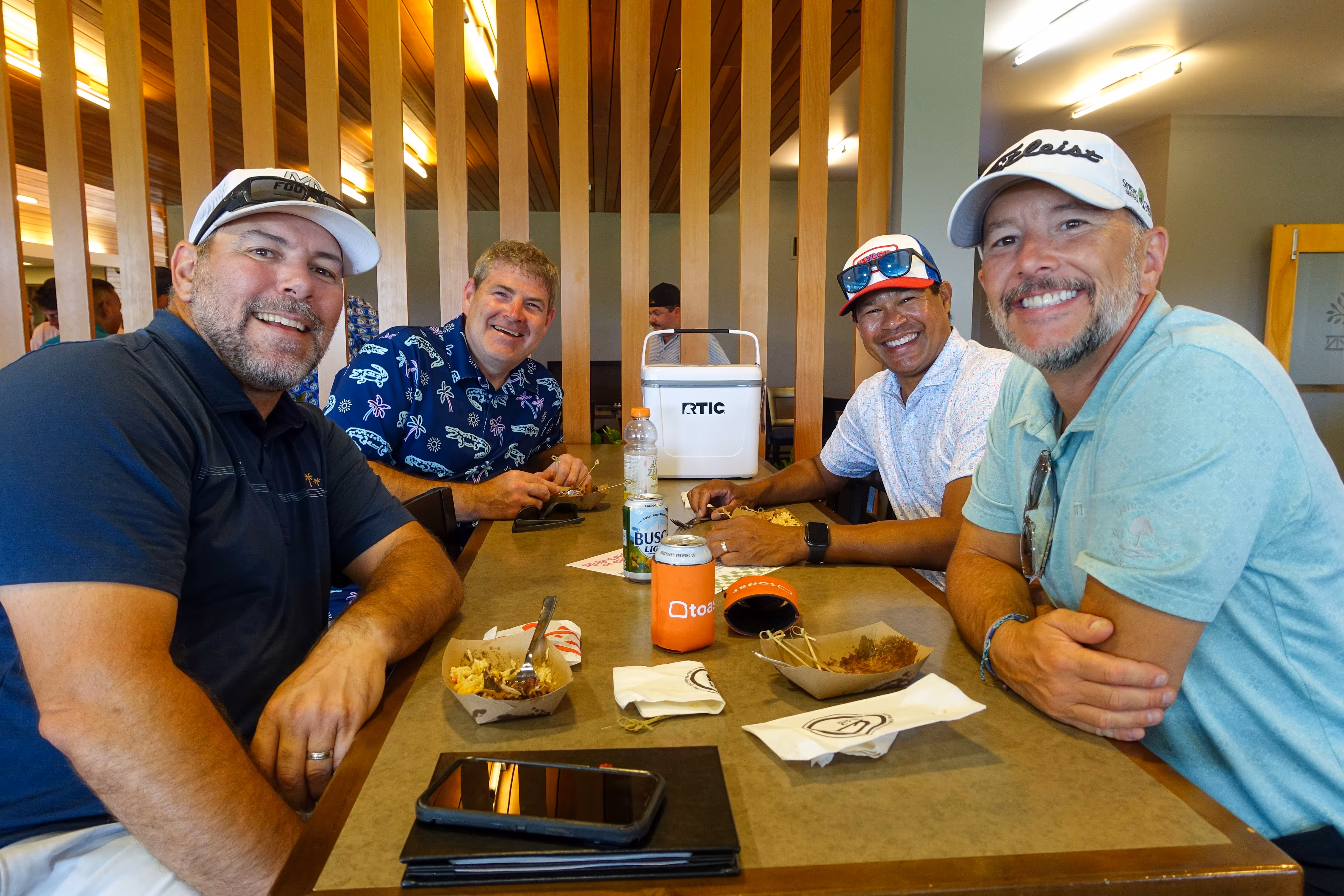 Group of people, including children and adults, gathered outdoors near a stage with some hugging and others standing nearby in casual summer clothing.