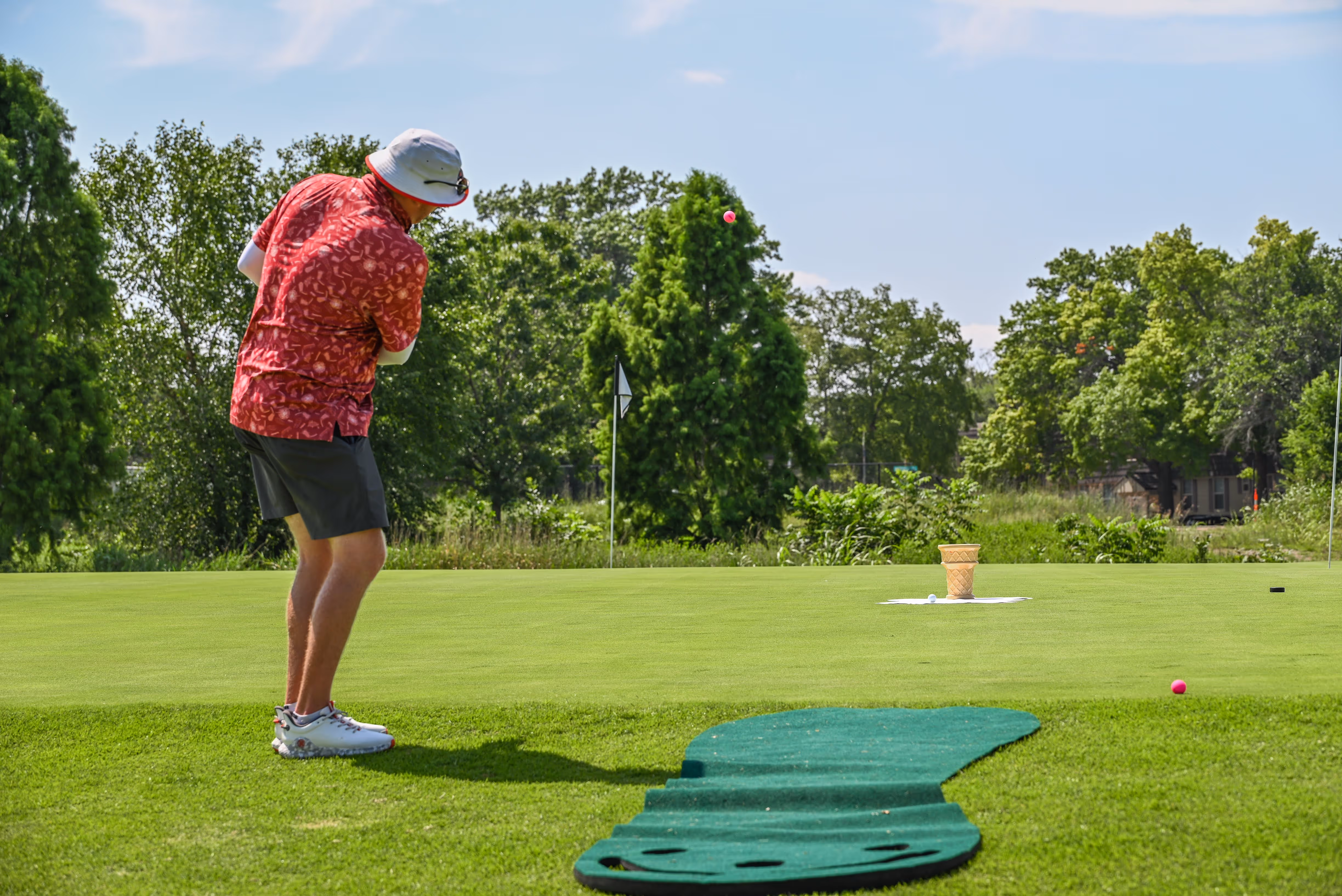 Group of people, including children and adults, gathered outdoors near a stage with some hugging and others standing nearby in casual summer clothing.