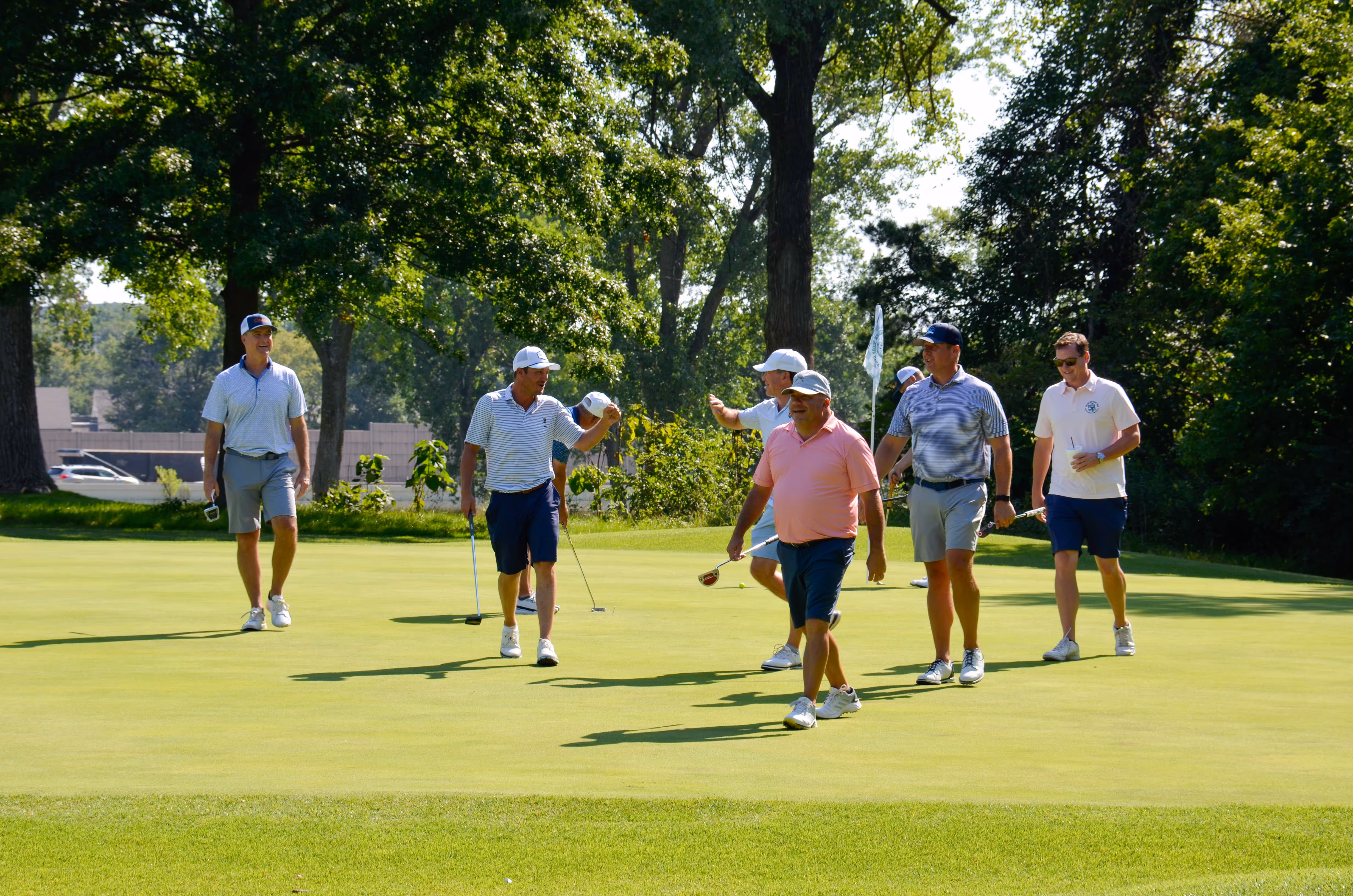 Group of people, including children and adults, gathered outdoors near a stage with some hugging and others standing nearby in casual summer clothing.