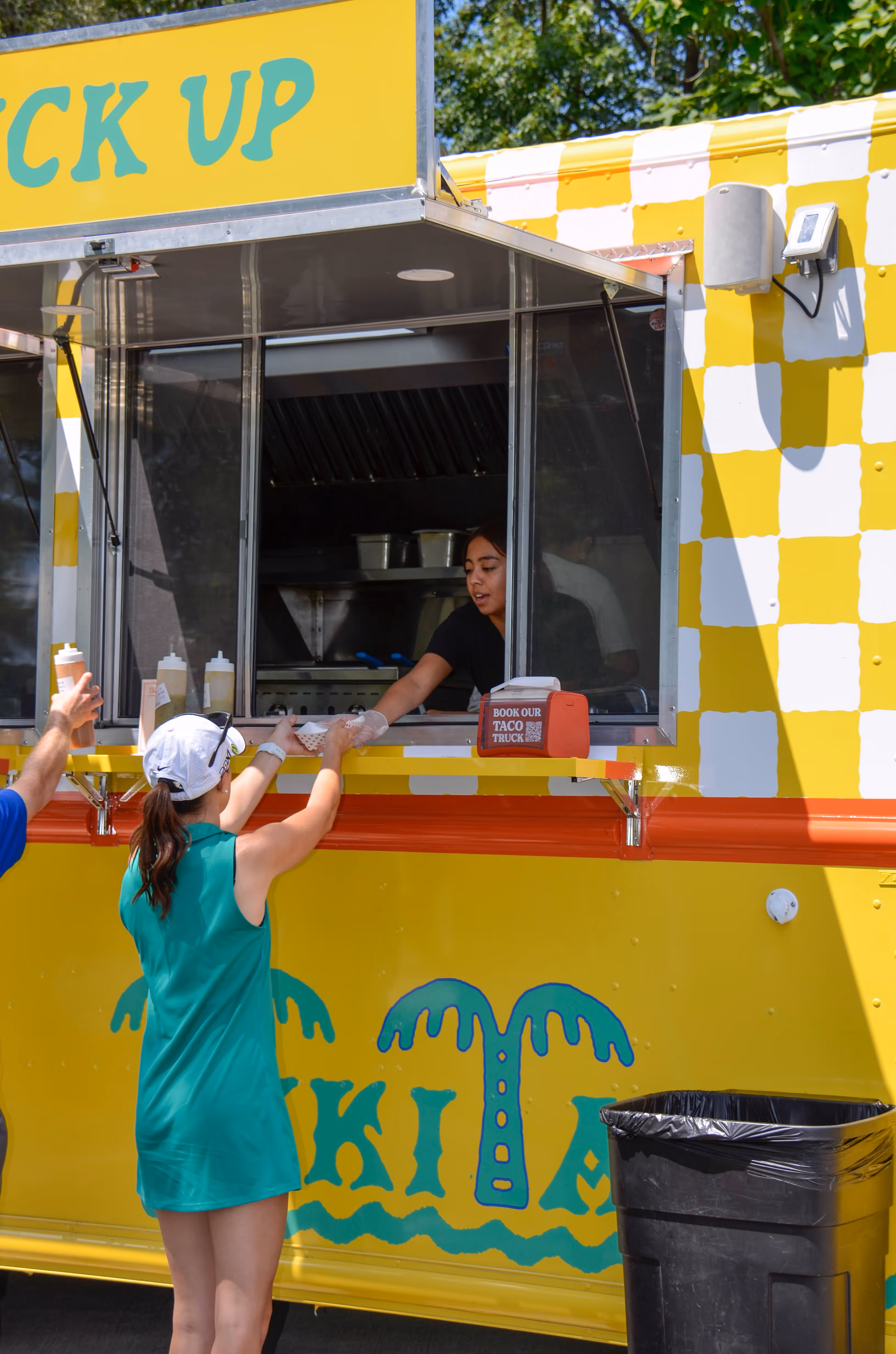 Group of people, including children and adults, gathered outdoors near a stage with some hugging and others standing nearby in casual summer clothing.