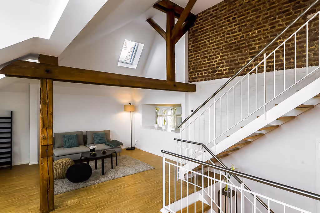 Modernes Loft mit offener Galerie, sichtbaren Holzbalken und rustikaler Backsteinwand im denkmalgeschützten Kloster „Guter Hirte“ in Aachen – Kombination aus historischem Charme und zeitgemäßem Wohnkomfort.