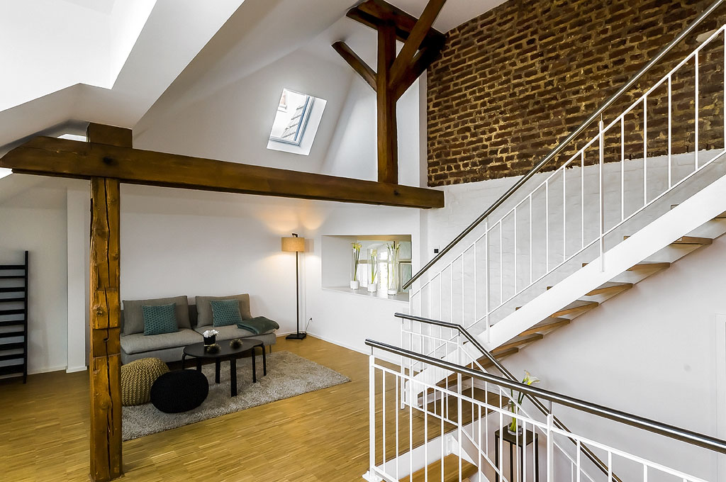Modernes Loft mit offener Galerie, sichtbaren Holzbalken und rustikaler Backsteinwand im denkmalgeschützten Kloster „Guter Hirte“ in Aachen – Kombination aus historischem Charme und zeitgemäßem Wohnkomfort.