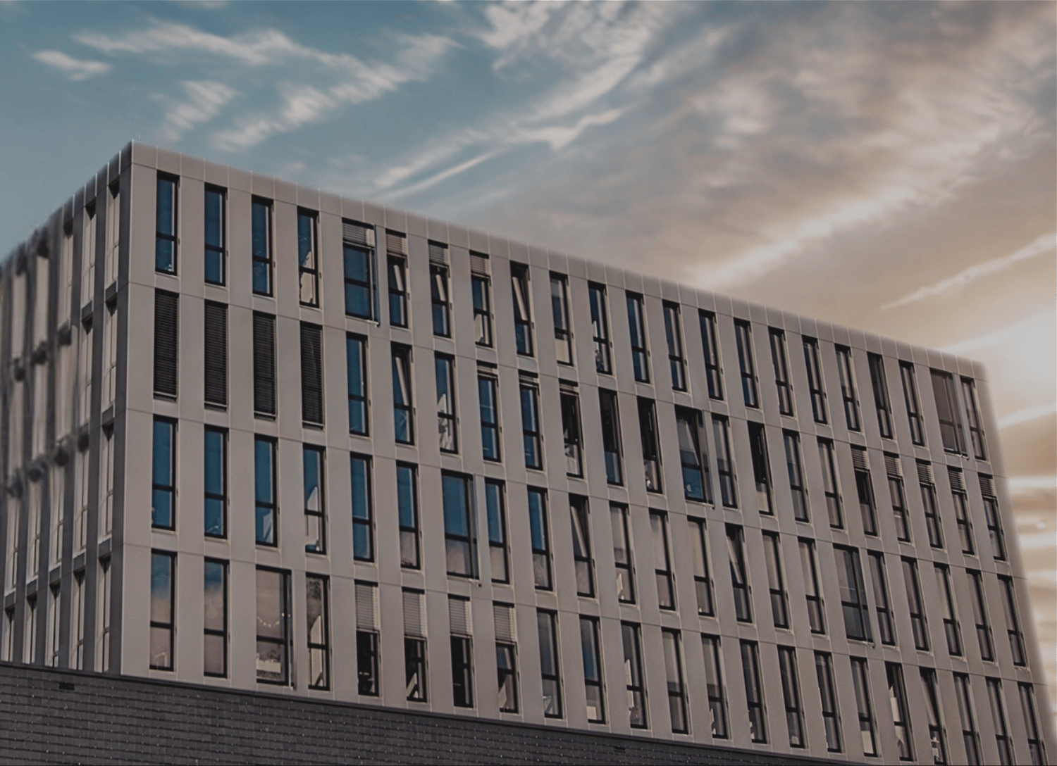 Modernes mehrstöckiges Gebäude der FH Aachen bei Sonnenuntergang mit zwei wehenden Fahnen.