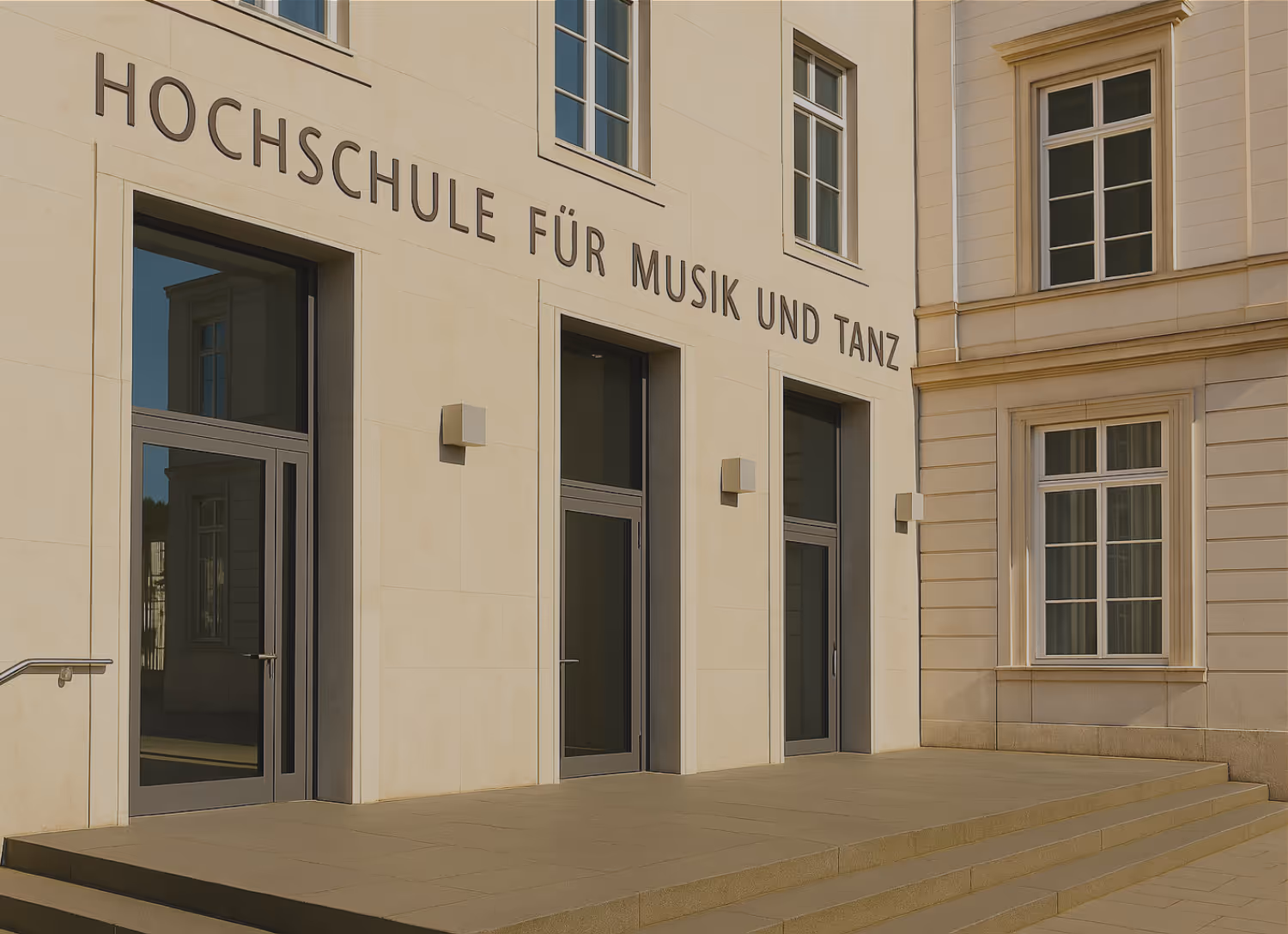 Gebäude der Hochschule für Musik und Tanz an einer Straßenecke mit geparkten Autos vor dem Eingang bei bewölktem Himmel.