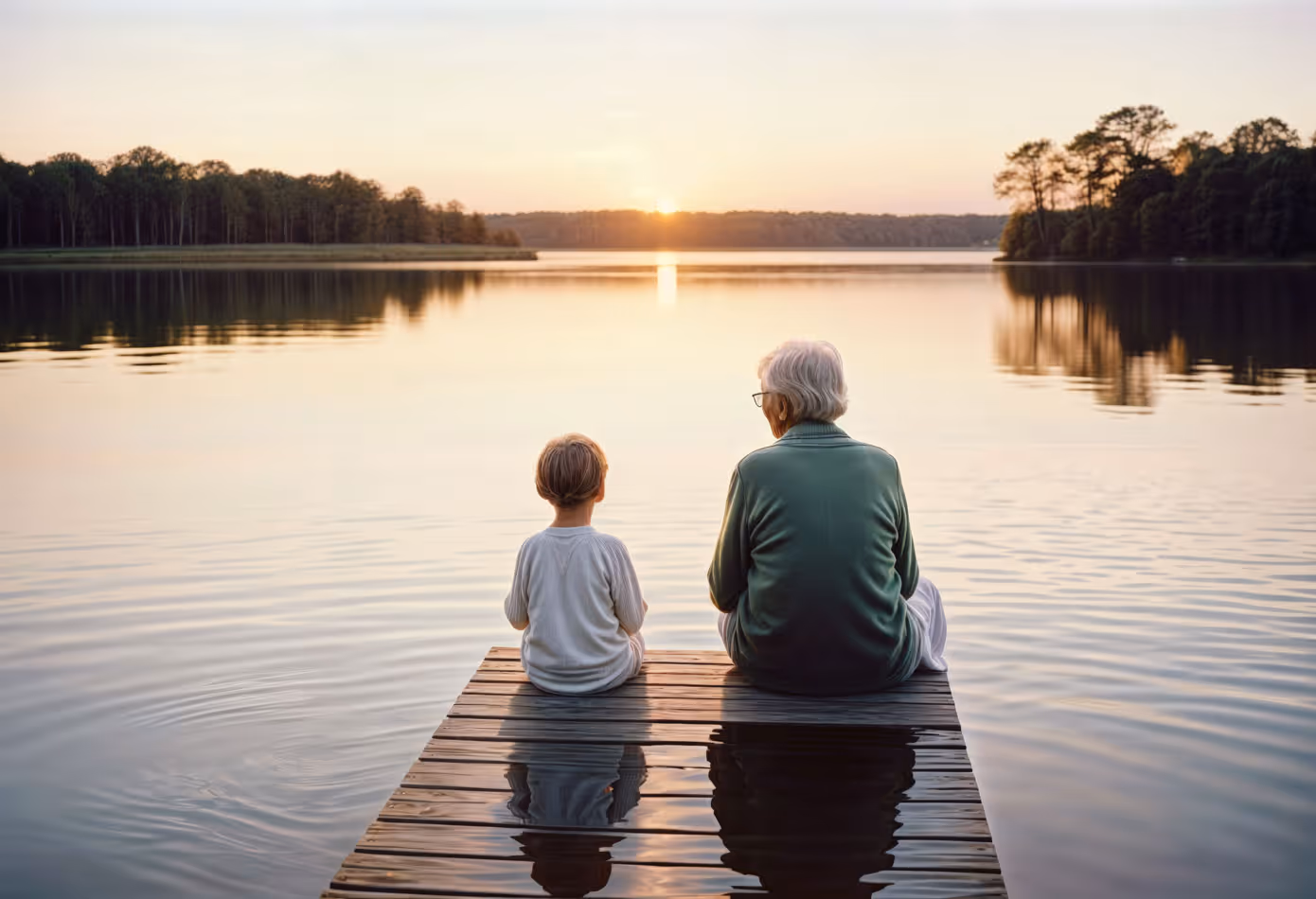 Grandfather and grandson sit on the dock and look out into the lake at sunset