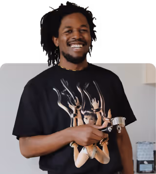 A cheerful Black man with dreadlocks and glasses smiles at the camera.