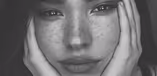 An artistic black-and-white close-up of a woman's face with freckles, looking directly into the camera.