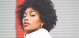 A stylish Black woman wearing a white top looks confidently sideways at the camera.