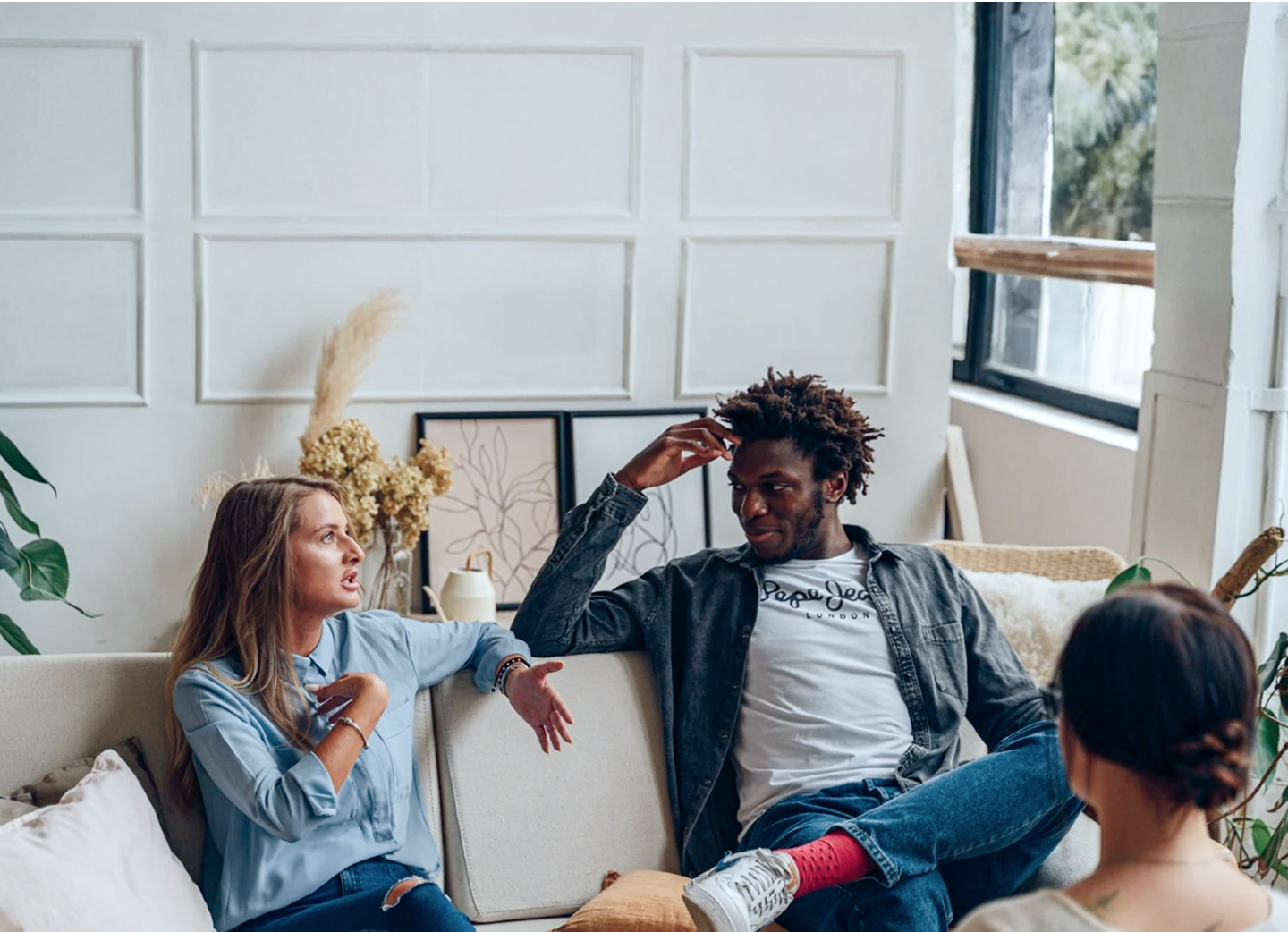 A diverse group of friends socializes and relaxes on a sofa in a modern living room.
