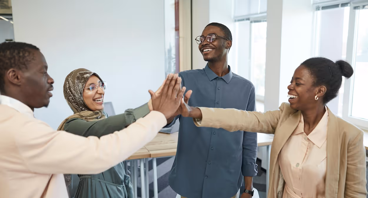 A diverse team of coworkers celebrates in a circle, joining their hands for a group high-five.