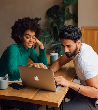 A man and a woman from different ethnic backgrounds laugh together while working on a laptop.