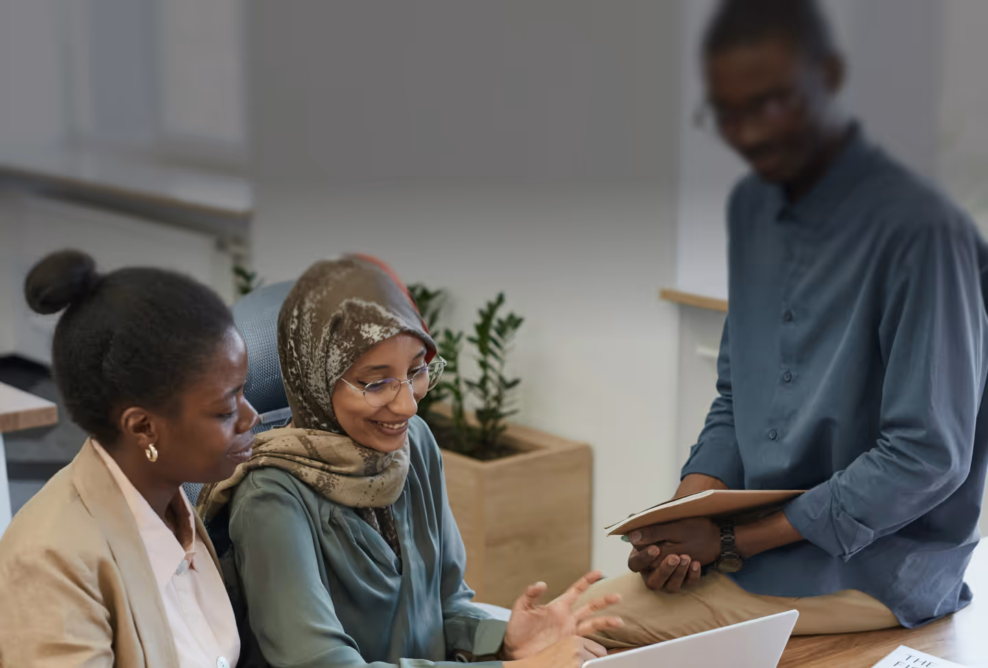A black man assists two women seated at the table staring at something out of frame.