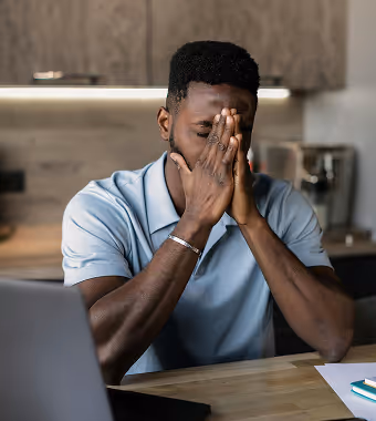 A man sits in front of his laptop with his head in his hands, appearing frustrated or overwhelmed.